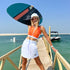 Wake surfer wearing a sleeveless cropped rash guard in orange colour colour with white panels.  